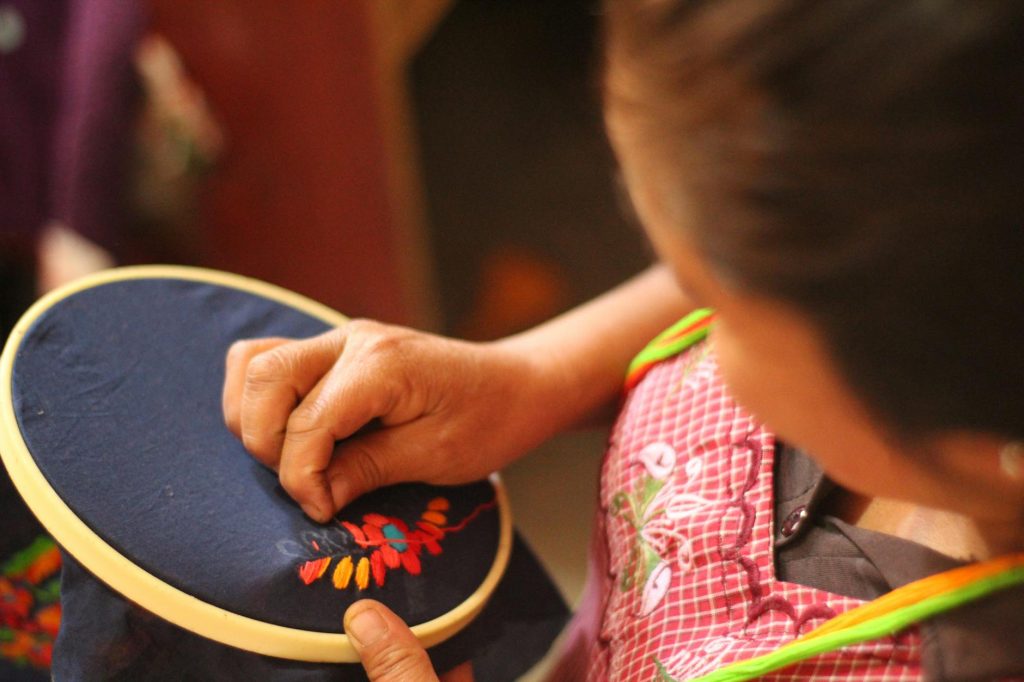A woman skillfully embroidering colorful patterns on fabric using a hoop, showcasing traditional craftsmanship.